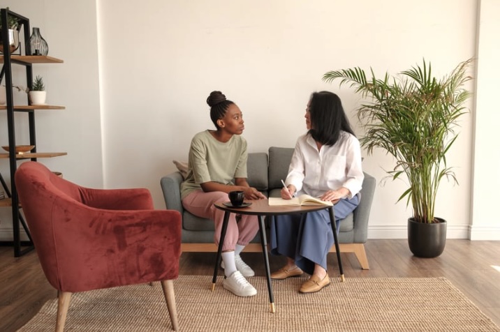 A therapist and client talk during an individual counseling session in Monmouth County, New Jersey. The meeting takes place in a calm, modern office with warm natural light, indoor plants, and comfortable seating that create a safe and supportive environment for therapy.