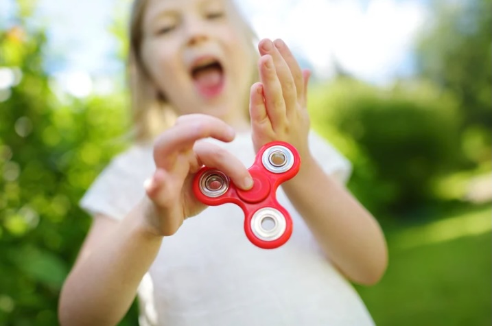 Child playing with a red fidget spinner outdoors, illustrating common ADHD behaviors for a therapy-focused blog serving families in Monmouth and Ocean County, New Jersey.