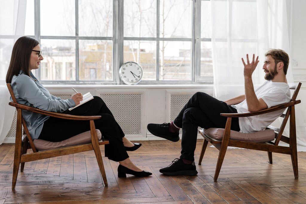 Therapist taking notes during an in-person exposure and response prevention therapy session with an adult client seated across from her in a bright office setting.